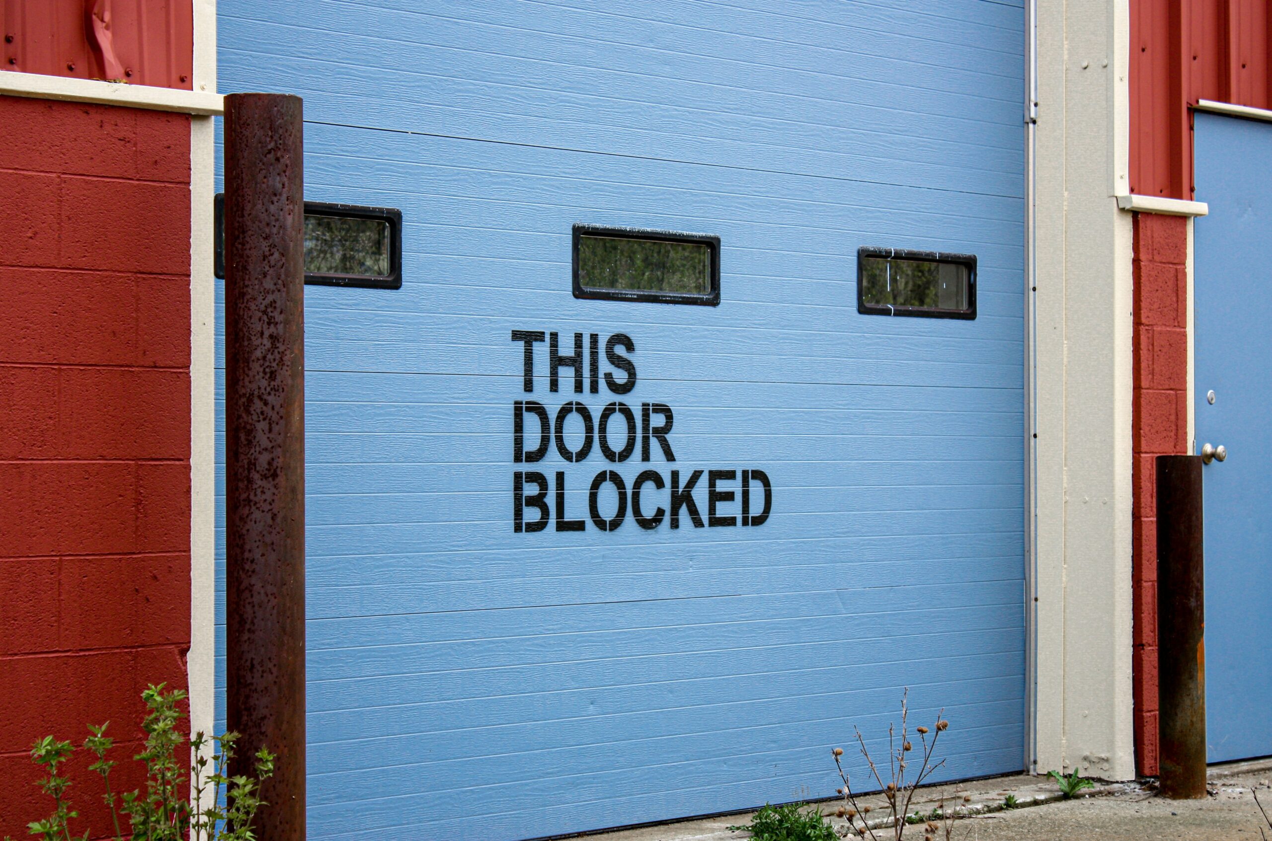 Porta del garage blu con la scritta "This Door blocked". Foto di Morgane Perraud su Unsplash